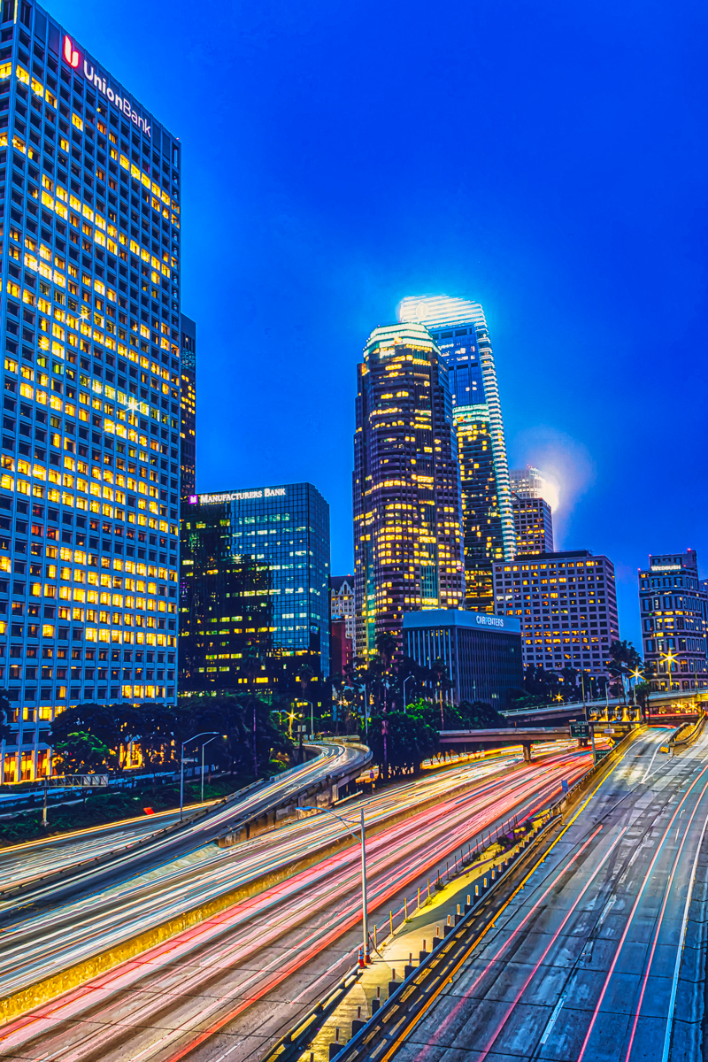 LA skyline and the 110 freeway at night — long-exposure light trails cutting through downtown